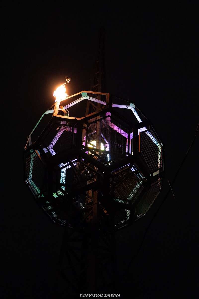 Close-up — buckyball with fire crown, panels lit in pink, green, and blue