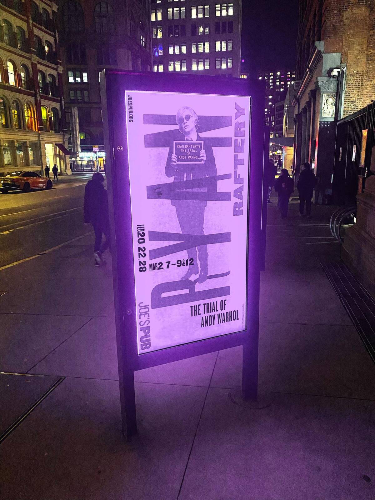 The Trial of Andy Warhol poster lit up on a NYC street kiosk at night